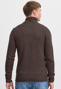 Brun strikket sweater med høj krave, ribstrikkede manchetter og kant, der har et struktureret mønster og en afslappet pasform.