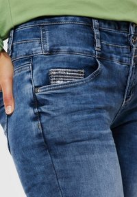 Blå denimjeans med en tajt passform, som har en liten, texturerad ficka och synliga sömnadsdetaljer. Slät tyg med lätt blekning.
