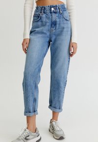 Jeans de mezclilla de cintura alta en azul claro con un corte relajado, que cuentan con un cierre de botón y cremallera, puños enrollados y un ligero desgaste.