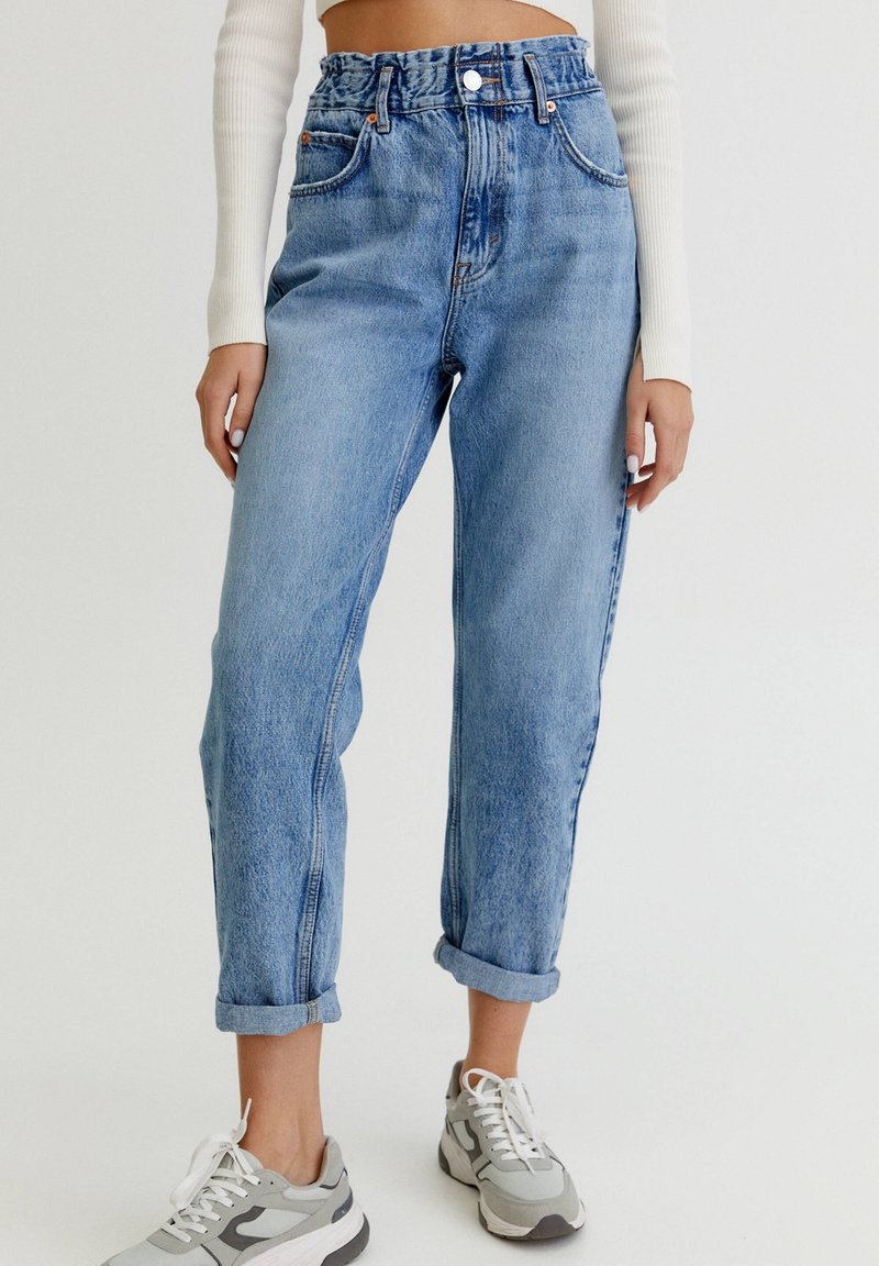 Jeans de mezclilla de cintura alta en azul claro con un corte relajado, que cuentan con un cierre de botón y cremallera, puños enrollados y un ligero desgaste.