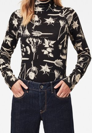 Un pull à col roulé à manches longues en coton noir avec des imprimés botaniques blancs, associé à un jean en denim foncé avec un bouton et des poches.