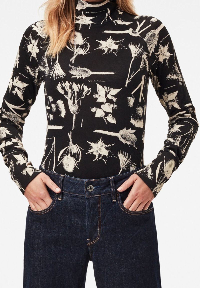 Langærmet turtleneck i sort bomuld med hvide botaniske prints, parret med mørke denim jeans med knap og lommer.