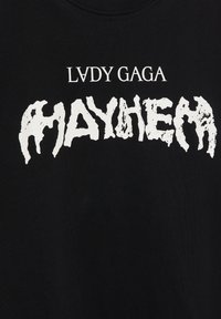 Mustat puuvillapaidat, joissa on rohkeaa valkoista tekstiä "LVDY GAGA MAYHEM" epätasaisella, rosoisella fontilla, korostaen graafista suunnittelua.