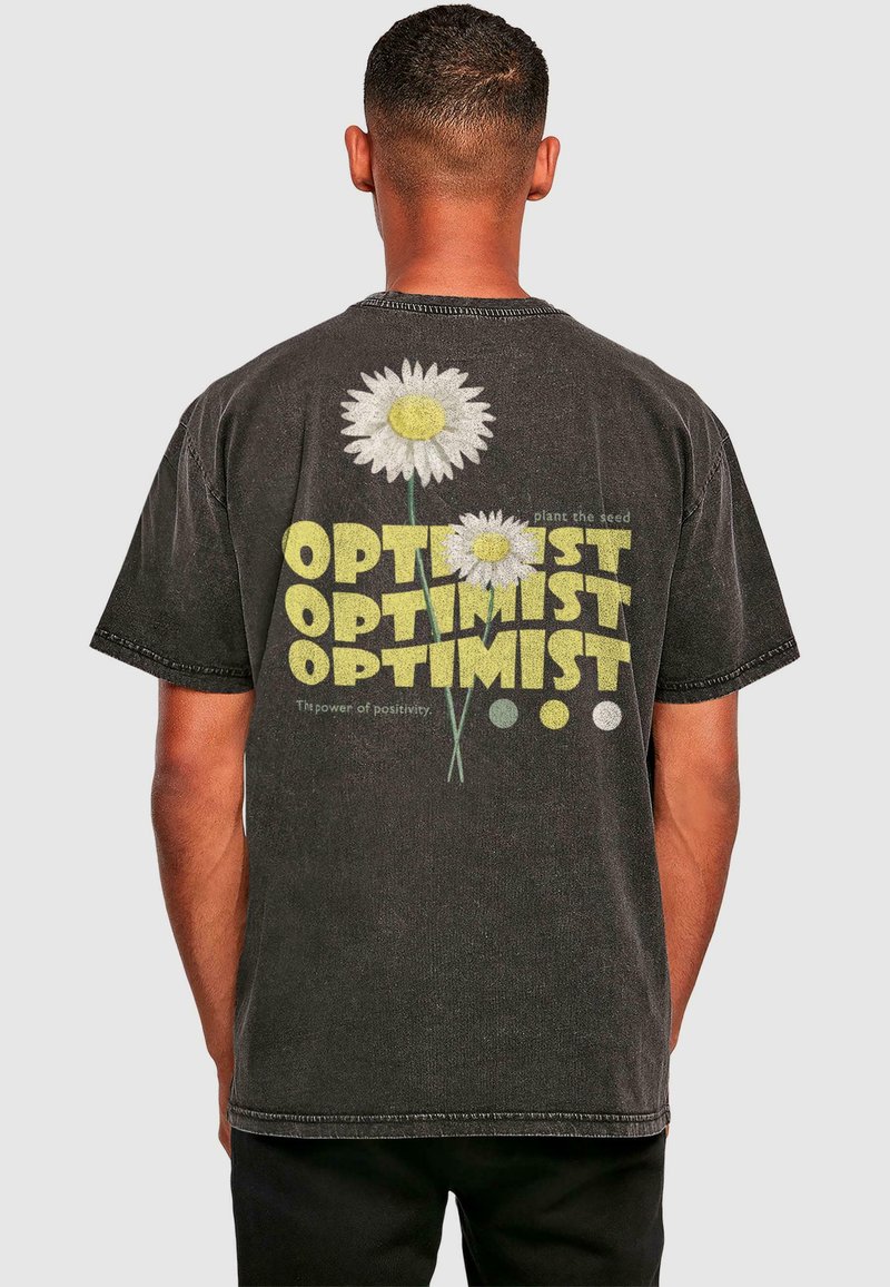 Schwarzes Baumwoll-T-Shirt mit großen weißen Gänseblümchen mit gelben Mittelpäckchen und dem Text "OPTIMIST" in verschiedenen Größen und Farben auf dem Rücken.