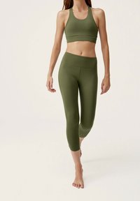 Grünes Sport-BH- und Capri-Leggings-Set aus glattem, dehnbarem Material. Es zeichnet sich durch ein figurnahes Design und einen minimalistischen Stil ohne sichtbare Muster aus.