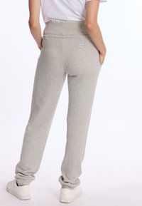 Grijze sweatpants van zacht materiaal, met een hoge tailleband en een logo-patch op de achterzak. Gestyled met witte sneakers.