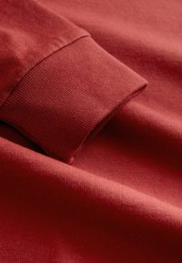 Nahaufnahme eines gefalteten roten Langarmhemds, das den Ärmel und die Stoffstruktur zeigt.