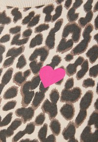 Tissu à imprimé léopard avec des taches sombres dispersées sur un fond beige et une petite forme de cœur rose vif imprimée près du centre.