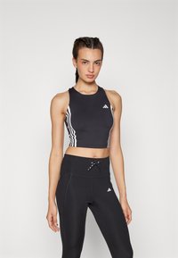 Svart crop-top med hvite vertikale striper og logo, parret med høyt liv svarte leggings som har snøring og logo detaljer.