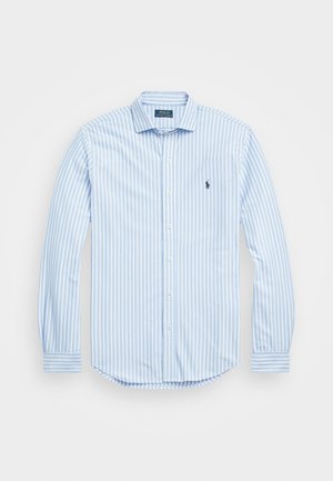 Chemise à manches longues rayée verticalement bleu clair et blanc avec des boutons et un petit logo brodé foncé sur la poitrine gauche.