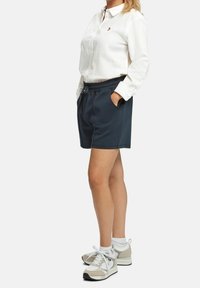 Vit skjorta med uppvikta ärmar, ihop med mörkblå shorts med resårmidja och sidofickor, bärs med ljusa sneakers.