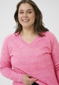 Ružový sveter s výstrihom do V, vyrobený z mäkkej, textúrovanej priadze a dlhými rukávmi, s jemným melírovaným vzorom a rebrovanými manžetami a lemom.