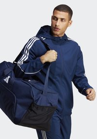 Marineblauwe sportjack met witte strepen en bijpassende sporttas. De tas heeft een gaasvak en stevige handvatten voor gemakkelijk dragen.