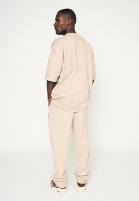 Camiseta de algodón beige de corte oversize y pantalones de chándal a juego con un ajuste relajado, que incluyen bolsillos y puños acanalados. Las zapatillas completan el look.