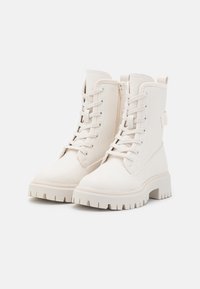 Białe botki za kostkę o teksturowanym wykończeniu, związywane z przodu, z bocznym zamkiem błyskawicznym i masywnymi, żłobionymi podeszwami dla lepszej przyczepności.