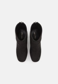Black suede ankle boots with a smooth texture, rounded toe, and a zipper detail at the back. Flat sole and minimalistic design.