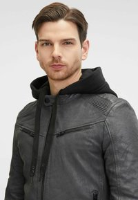 Giacca in pelle grigia con cappuccio, presenta tasche con cerniera, spalle testurizzate e lacci neri. Design casual con una vestibilità slim.