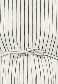 Tissu blanc à fines rayures verticales noires, avec un détail de ceinture nouée au centre. La texture semble légèrement froissée.