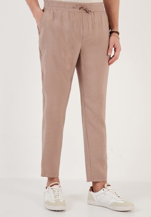 Lightweight, beige drawstring trousers with elastic waistband. Features side pockets and tapered legs, paired with white and beige sneakers.