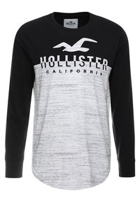 Mustat ja harmaat pitkähihaiset t-paidat, joissa on pyöreä kaula-aukko, ja jotka esittävät vaakasuoraa raidallista kuviointia sekä "Hollister California" -tekstiä paksuilla kirjaimilla.