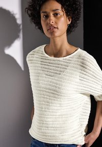 Helles crèmefarbenes Strickoberteil mit horizontalen Streifen, lockerer Passform, rundem Halsausschnitt und seitlichen Schlitzen. Kombiniert mit blauer Denim, die eine weiche Textur aufweist.
