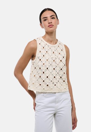 Top sans manches en crochet crème avec découpes florales, col rond et ourlet en feston ; associé à un pantalon blanc.