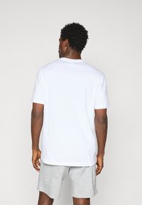 Weißes Baumwoll-T-Shirt mit kurzen Ärmeln, rundem Halsausschnitt und lockerer Passform, kombiniert mit grauen Shorts. Rückenansicht.