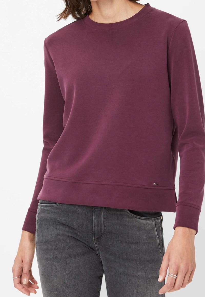 Sweat-shirt bordeaux en tissu doux, doté d'un col rond, de manches longues et d'un ourlet légèrement court. Design minimaliste avec un petit logo.