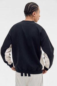 Schwarzer Sweatshirt mit cremefarbenen Seitenpanelen, gerippten Bündchen und Saum. Weiche Textur mit lässigem Schnitt. Die Rückansicht zeigt einen geflochtenen Haarschnitt.