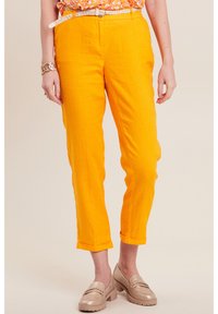 Helle orange Leinenhosen mit geradem Schnitt, umgeschlagenen Säumen und strukturiertem Finish, kombiniert mit hellen Schuhen.