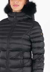 Giacca a vento nera con design trapuntato, colletto alto e cappuccio in pelliccia staccabile. Chiusura con zip e tasche laterali. Tessuto liscio e lucido.