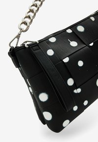 Borsa in tessuto nero con pois bianchi, dotata di una superficie testurizzata e una tracolla in catena metallica. Forma strutturata con pattina pieghevole.