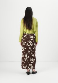 Haut à manches longues texturé vert associé à une jupe maxi à motifs floraux marron. Des chaussures à brides noires complètent la tenue.