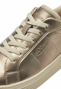 Zapatilla metálica bronce con cordones beige, que presenta una parte superior de cuero texturizado y una suela de goma blanca. Logo "s.Oliver" en el costado.