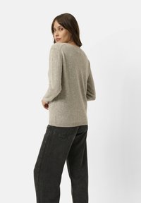 Maglione grigio chiaro a maglia con scollo rotondo e maniche lunghe, abbinato a jeans neri a gamba larga. Texture morbida visibile. Design semplice.