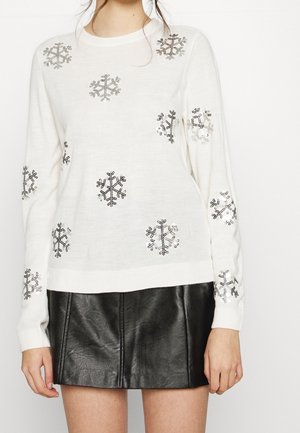 Maglione bianco lavorato a maglia con ricamo di fiocchi di neve argento e neri. Maniche lunghe e polsini a coste. Abbinato a una gonna di pelle nera.