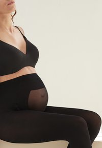 Bra da maternità nero con texture liscia e scollatura a V, abbinato a leggings neri opachi con un pannello trasparente sulla pancia.