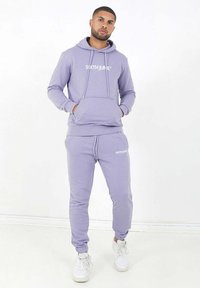 Sudadera lila con bolsillo frontal y cordones, combinada con pantalones de chándal a juego. Ambos presentan el logo "SIXTHJUNE" en blanco en el pecho y en la pierna.