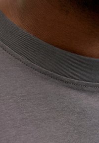 Siva majica s kratkimi rokavi in rebrastim okroglim izrezom, izdelana iz gladkega bombažnega blaga. Na njej je subtilna tekstura in čisti šivi vzdolž robov.