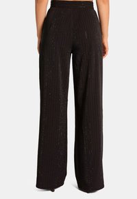 Zwarte wijde broek met verticale strepen, voorzien van een textuur en subtiele schitteringen voor extra detail. Verstelbare tailleband.