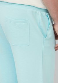 Jogging en bleu clair en tissu doux, avec une poche arrière et une taille élastique. Texture lisse et design décontracté.