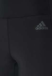 Mustat urheilulegginsit, jotka on valmistettu sileästä ja joustavasta materiaalista. Ominaisuuksiin kuuluu saumaton muotoilu ja pieni harmaa Adidas-logo sivussa.