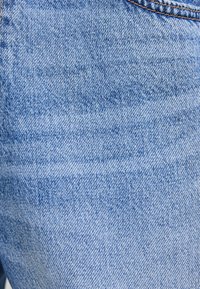 Ljusblå denimtyg med en subtil textur, som har en klassisk twillväv och synliga sömdetaljer. Inga utsmyckningar eller mönster.