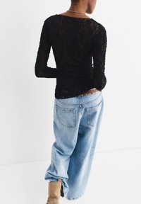 Schwarzes Spitzenshirt mit langen Ärmeln und figurbetontem Schnitt, kombiniert mit lockeren hellblauen Jeans und braunen Knöchelstiefeln.