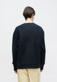 Μπλε ναυτικό φούτερ με στρογγυλή λαιμόκοψη, άνετη εφαρμογή, ριμπ μανσέτες και τελείωμα, απεικονίζεται από πίσω. Ομαλή υφή, ελάχιστες λεπτομέρειες σχεδίασης.