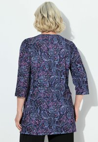Tunic con motivo paisley nelle tonalità blu navy, viola e rosa. Presenta maniche a tre quarti e una vestibilità rilassata; il tessuto appare liscio e leggero.