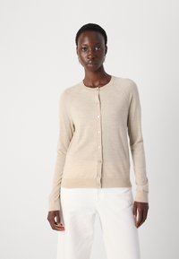Beige cardigan med rund halsringning, långa ärmar och knappstängning fram. Har en mjuk textur och en lätt figurnära design.