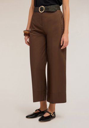 Pantalons marron à jambes larges avec une ceinture noire texturée ornée d'une boucle en or. Chaussures plates noires avec découpes rondes et accent doré.