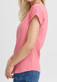 T-shirt rose à manches courtes en coton doux, avec une coupe décontractée et un col rond, associé à un jean en denim bleu.