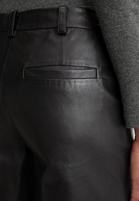 Schwarze Lederhosen mit einem eleganten Design, glatter Textur und einer Gesäßtasche mit geradem Öffnungsstil. Gürtelschlaufen an der Taille.